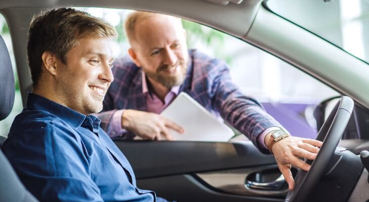 Man sits in vehicle as salesman shows him the features