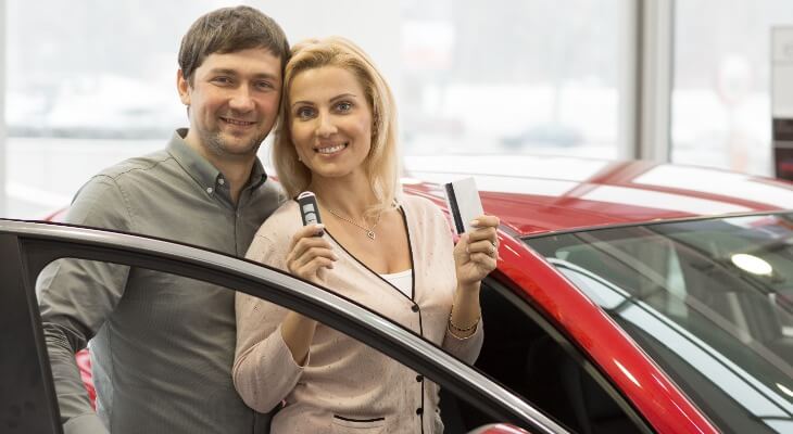 New car discount: Couple smiles in front of a red car