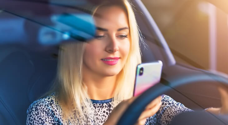 Low mileage discount state farm: woman using her phone while driving a car
