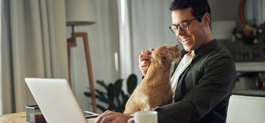 man smiling while petting his dog and looking at the computer