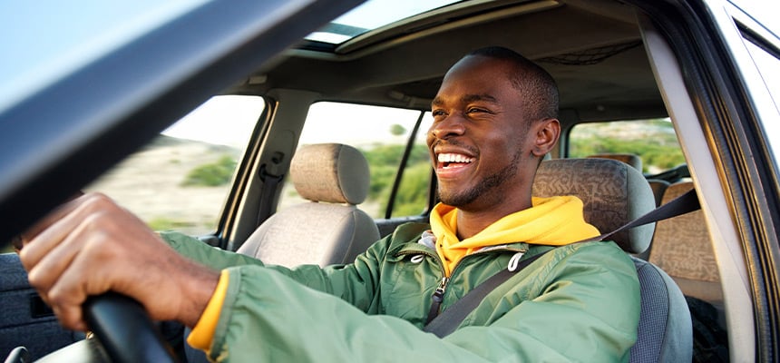 Man in green driving a car and smiling.