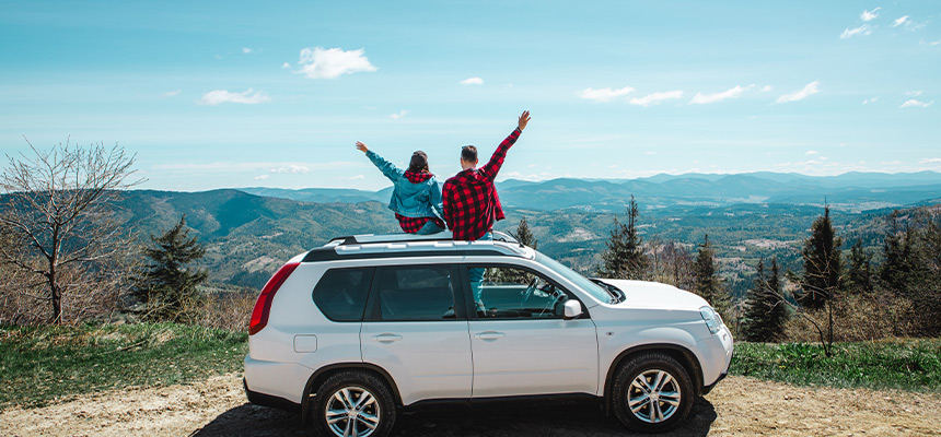 Two people sitting on the top of a white SUV, waving their hands